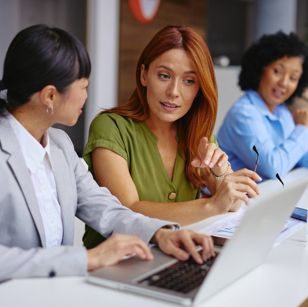 A sales manager coaches a colleague at a laptop while a teammate looks on.
