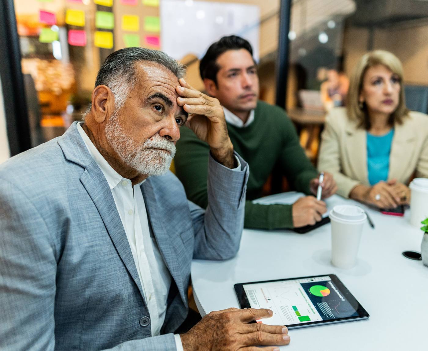 A sales leader rubs his forehead during a tense team meeting while colleagues look on.